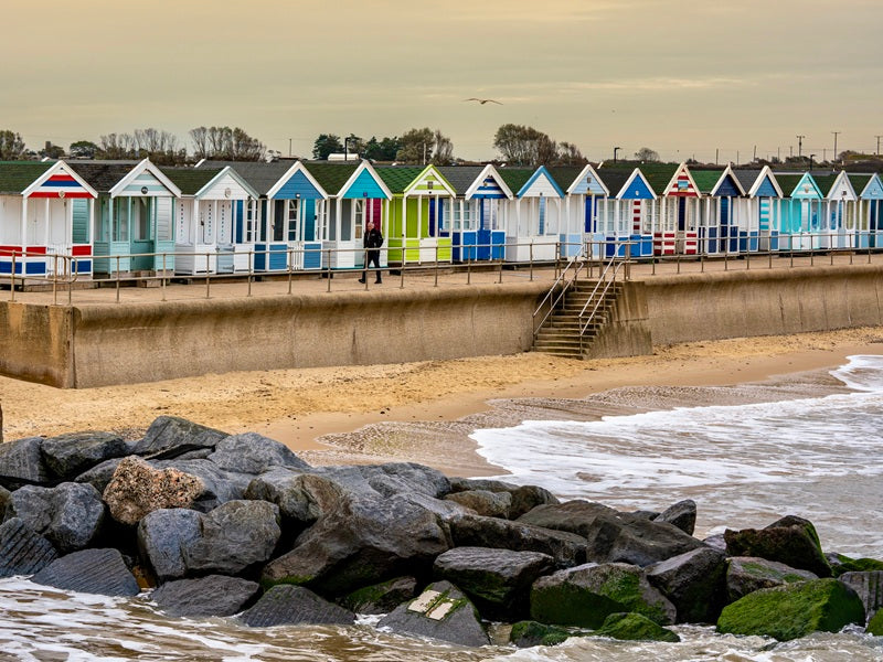 Colorful beach huts along a coastal path with rocks and water in the foreground.
