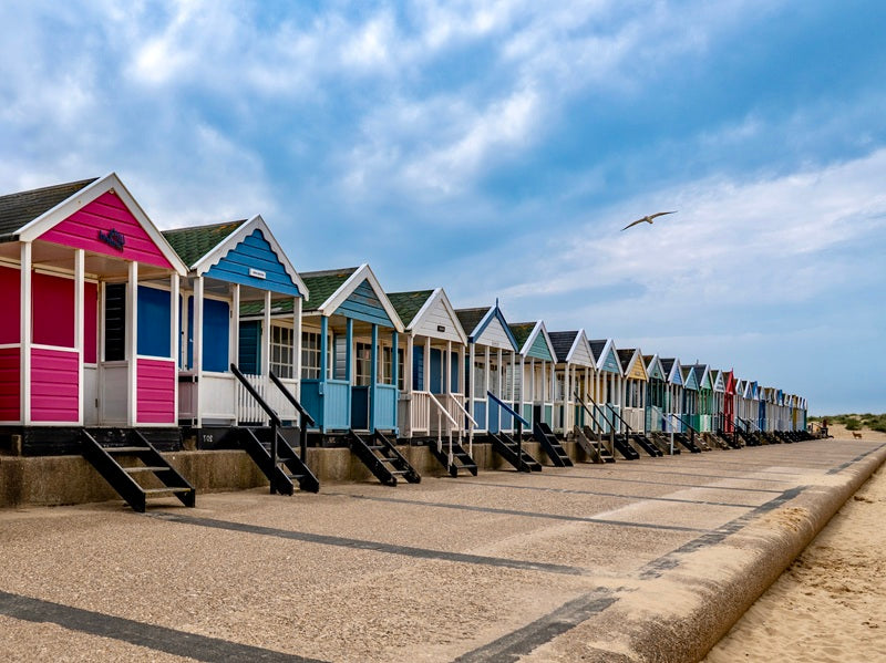 Row of colorful beach huts on a sandy beach with a clear blue sky.