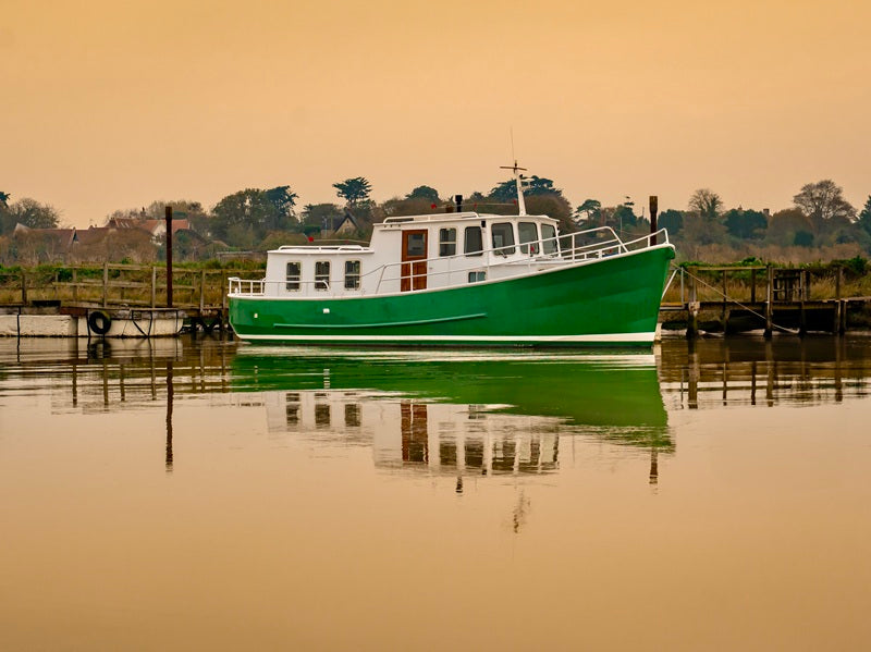 A peaceful photograph of a wooden boat moored on calm water during a soft sunset, coastal wall art by Suzanne Morshead